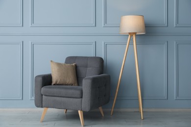 Photo of Comfortable armchair and lamp near light blue wall indoors
