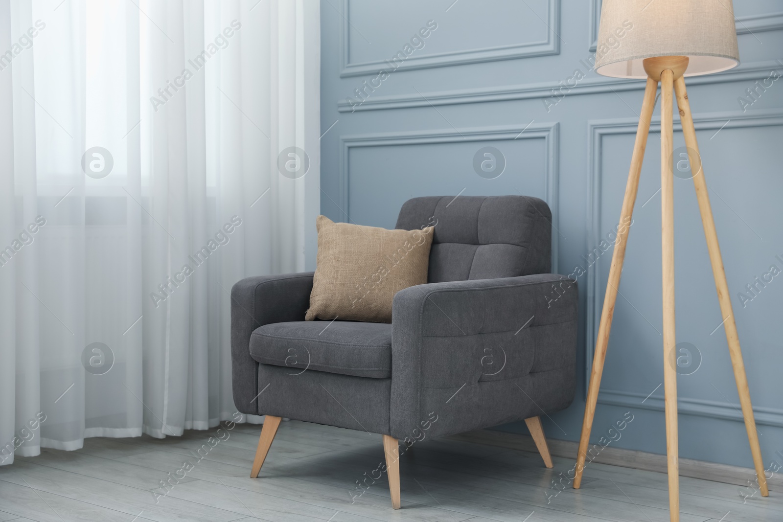 Comfortable armchair and lamp near light blue wall indoors Photo of Comfortable armchair and lamp near light blue wall indoors