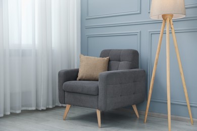 Photo of Comfortable armchair and lamp near light blue wall indoors