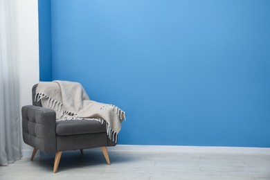 Photo of Comfortable armchair with plaid near blue wall indoors. Space for text