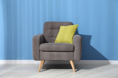 Photo of Comfortable armchair with cushion near blue wall indoors