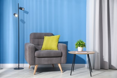 Photo of Comfortable armchair, lamp and houseplant near blue wall indoors