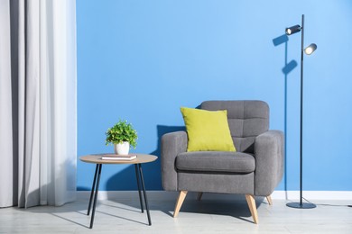 Photo of Comfortable armchair, lamp and houseplant near blue wall indoors