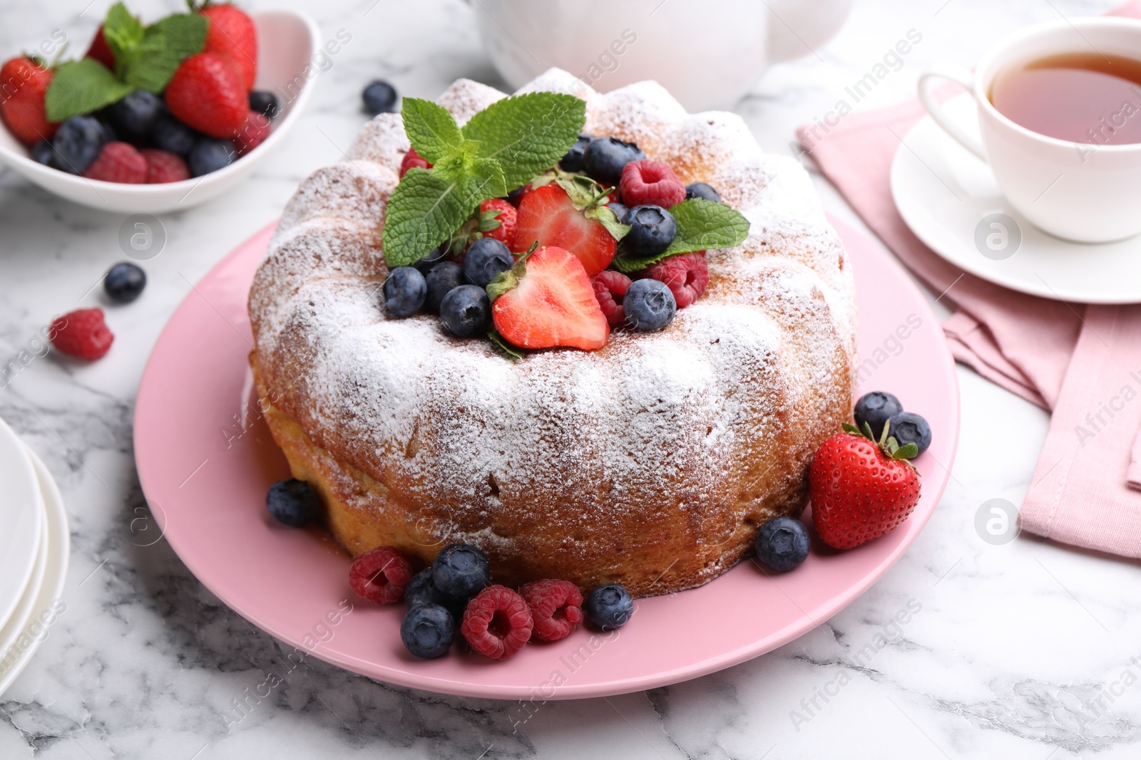 Photo of Tasty Bundt cake with powdered sugar and berries on white marble table, closeup