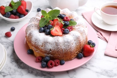 Photo of Tasty Bundt cake with powdered sugar and berries on white marble table, closeup