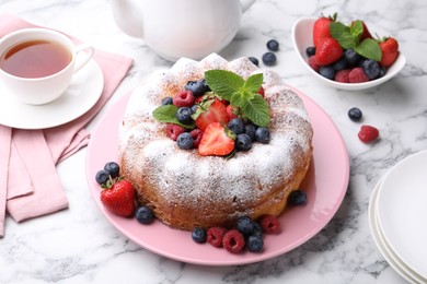 Photo of Tasty Bundt cake with powdered sugar and berries on white marble table