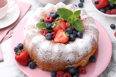 Photo of Tasty Bundt cake with powdered sugar and berries on white marble table, closeup
