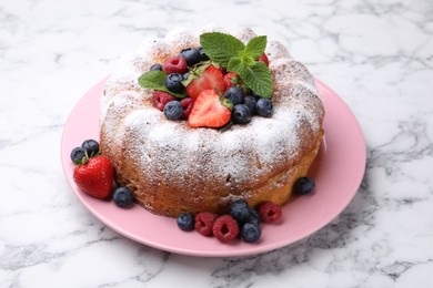 Photo of Tasty Bundt cake with powdered sugar and berries on white marble table, closeup