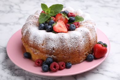 Photo of Tasty Bundt cake with powdered sugar and berries on white marble table, closeup