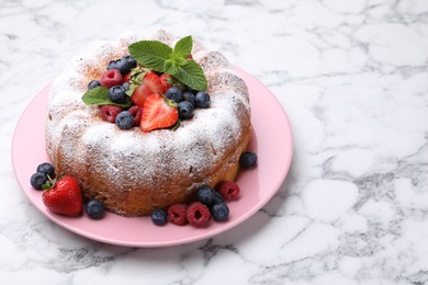 Photo of Tasty Bundt cake with powdered sugar and berries on white marble table, space for text