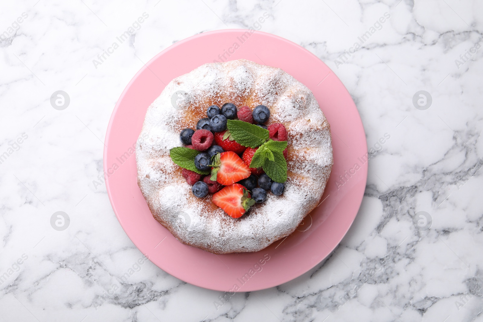 Photo of Tasty Bundt cake with powdered sugar and berries on white marble table, top view