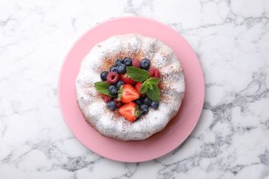 Photo of Tasty Bundt cake with powdered sugar and berries on white marble table, top view