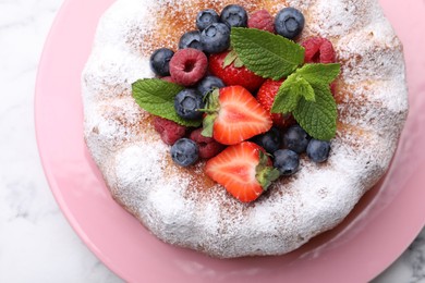 Photo of Tasty Bundt cake with powdered sugar and berries on white marble table, top view