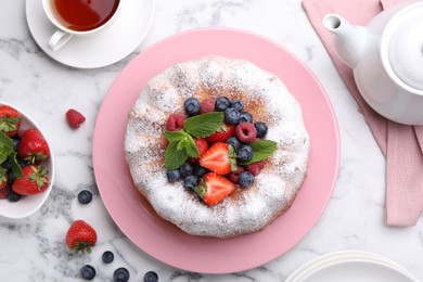 Photo of Tasty Bundt cake with powdered sugar and berries on white marble table, flat lay