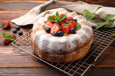 Photo of Tasty Bundt cake with powdered sugar and berries on wooden table, closeup