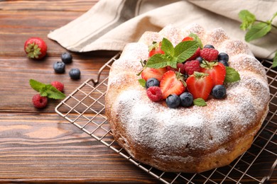 Photo of Tasty Bundt cake with powdered sugar and berries on wooden table, closeup