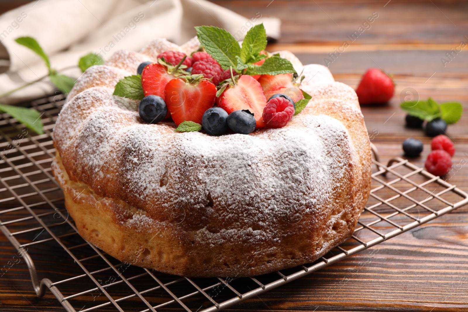 Tasty Bundt cake with powdered sugar and berries on wooden table, closeup Photo of Tasty Bundt cake with powdered sugar and berries on wooden table, closeup