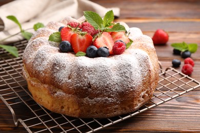 Photo of Tasty Bundt cake with powdered sugar and berries on wooden table, closeup