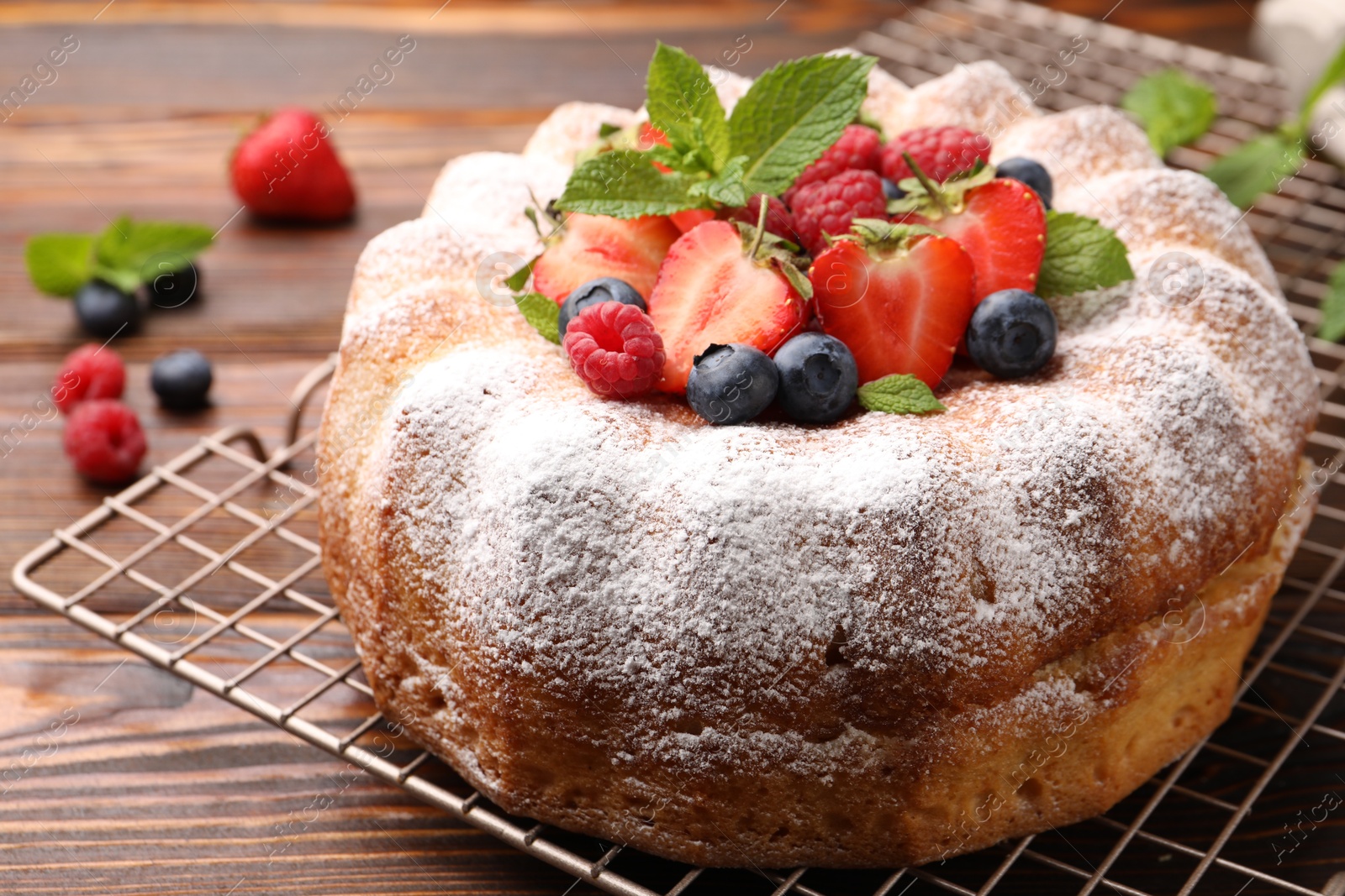 Photo of Tasty Bundt cake with powdered sugar and berries on wooden table, closeup