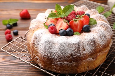 Photo of Tasty Bundt cake with powdered sugar and berries on wooden table, closeup