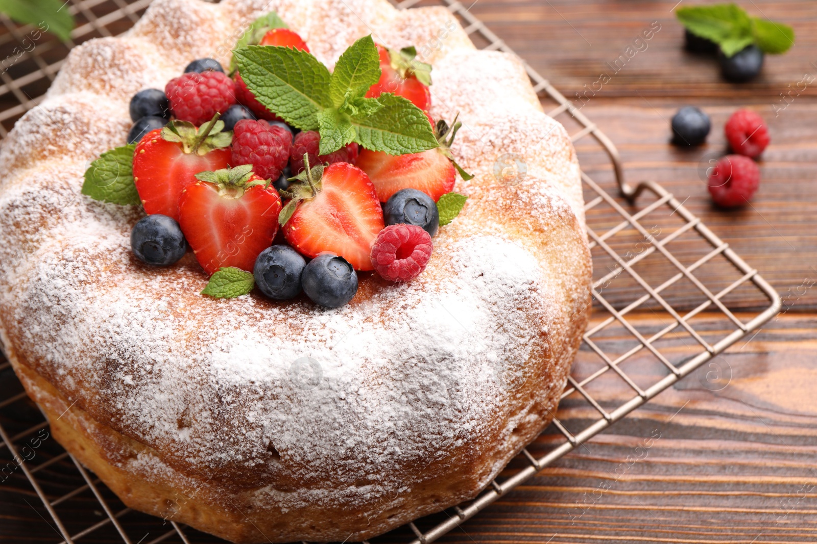 Tasty Bundt cake with powdered sugar and berries on wooden table, closeup Photo of Tasty Bundt cake with powdered sugar and berries on wooden table, closeup