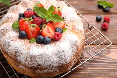 Photo of Tasty Bundt cake with powdered sugar and berries on wooden table, closeup