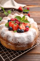 Photo of Tasty Bundt cake with powdered sugar and berries on wooden table, closeup