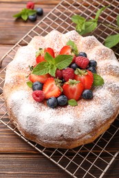Photo of Tasty Bundt cake with powdered sugar and berries on wooden table, closeup