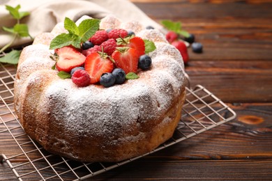 Photo of Tasty Bundt cake with powdered sugar and berries on wooden table, closeup. Space for text