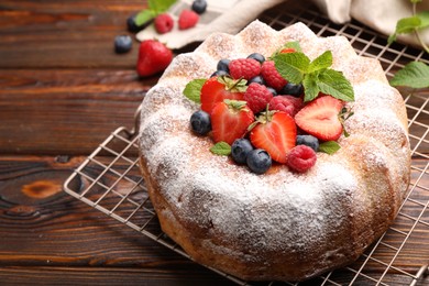 Photo of Tasty Bundt cake with powdered sugar and berries on wooden table, closeup. Space for text