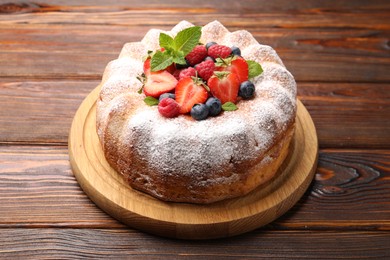 Photo of Tasty Bundt cake with powdered sugar and berries on wooden table