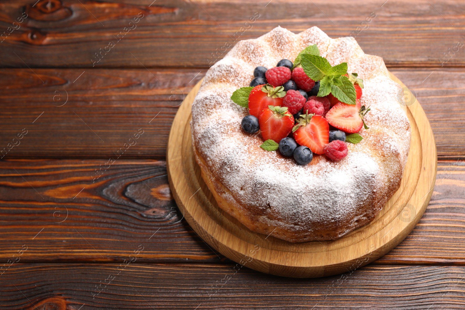 Photo of Tasty Bundt cake with powdered sugar and berries on wooden table, space for text