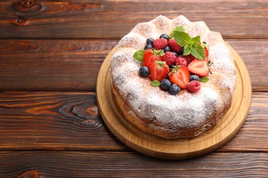 Photo of Tasty Bundt cake with powdered sugar and berries on wooden table, space for text