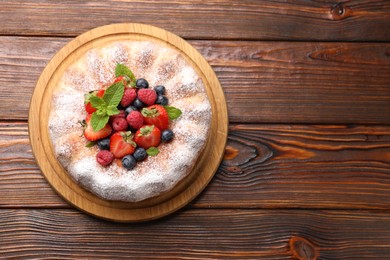 Photo of Tasty Bundt cake with powdered sugar and berries on wooden table, top view. Space for text