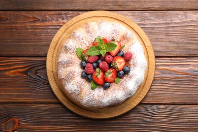 Photo of Tasty Bundt cake with powdered sugar and berries on wooden table, top view