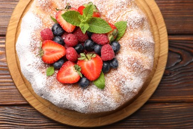 Photo of Tasty Bundt cake with powdered sugar and berries on wooden table, top view