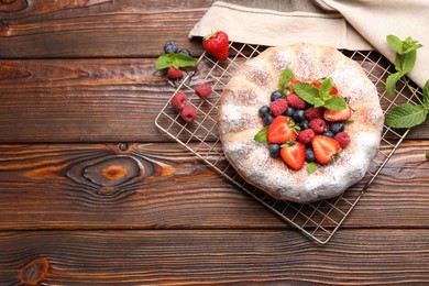 Photo of Tasty Bundt cake with powdered sugar and berries on wooden table, flat lay. Space for text
