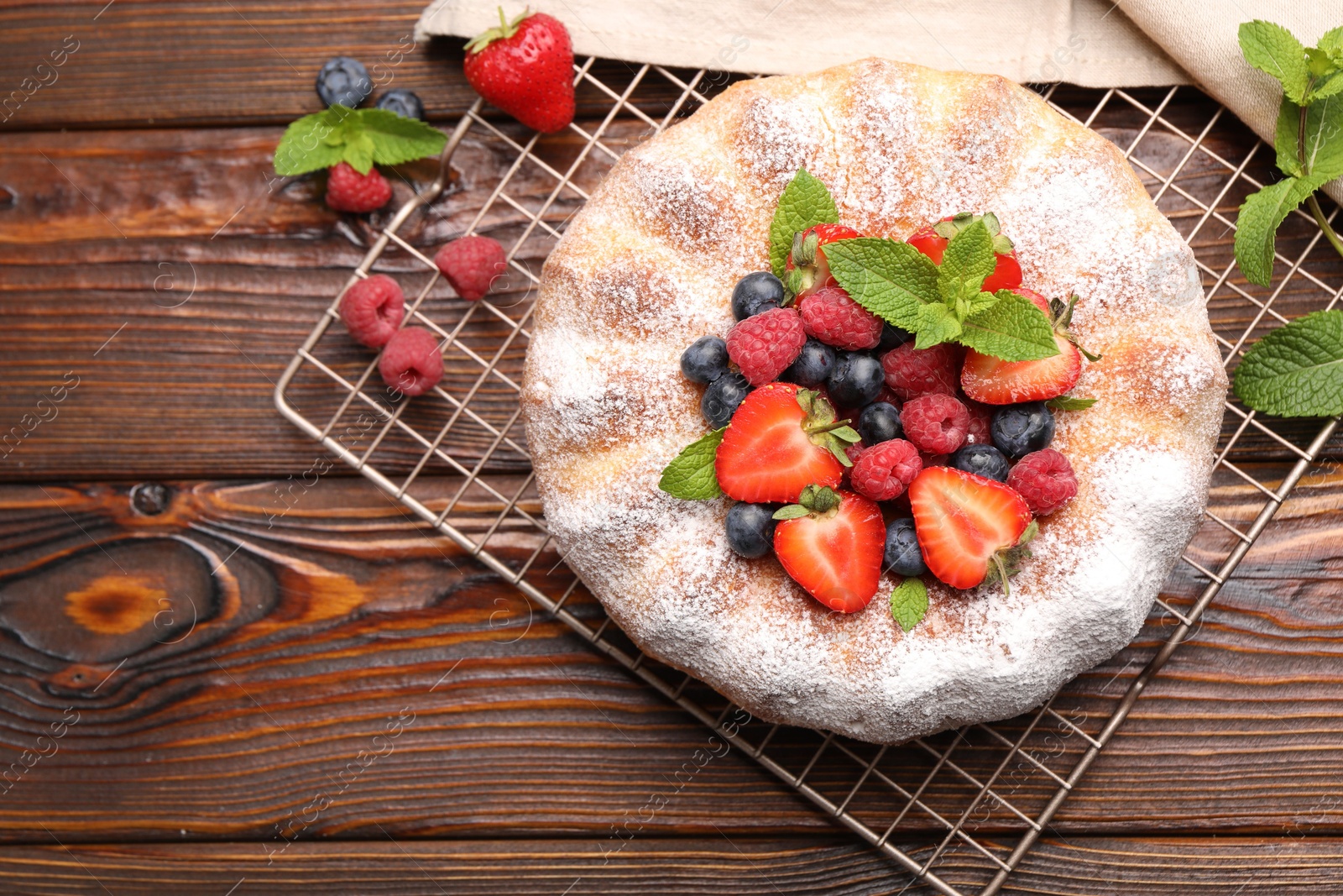 Photo of Tasty Bundt cake with powdered sugar and berries on wooden table, flat lay. Space for text