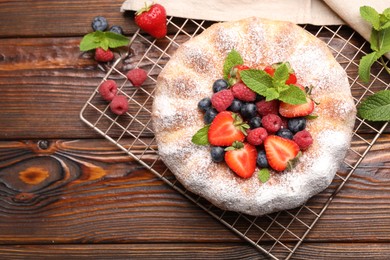 Photo of Tasty Bundt cake with powdered sugar and berries on wooden table, flat lay. Space for text