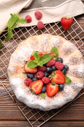 Photo of Tasty Bundt cake with powdered sugar and berries on wooden table, flat lay