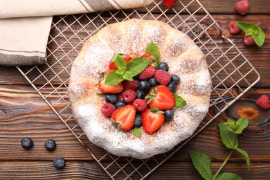 Photo of Tasty Bundt cake with powdered sugar and berries on wooden table, flat lay