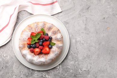 Photo of Tasty Bundt cake with powdered sugar and berries on grey textured table, top view. Space for text