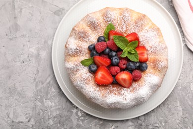 Photo of Tasty Bundt cake with powdered sugar and berries on grey textured table, top view
