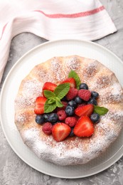Photo of Tasty Bundt cake with powdered sugar and berries on grey textured table, top view