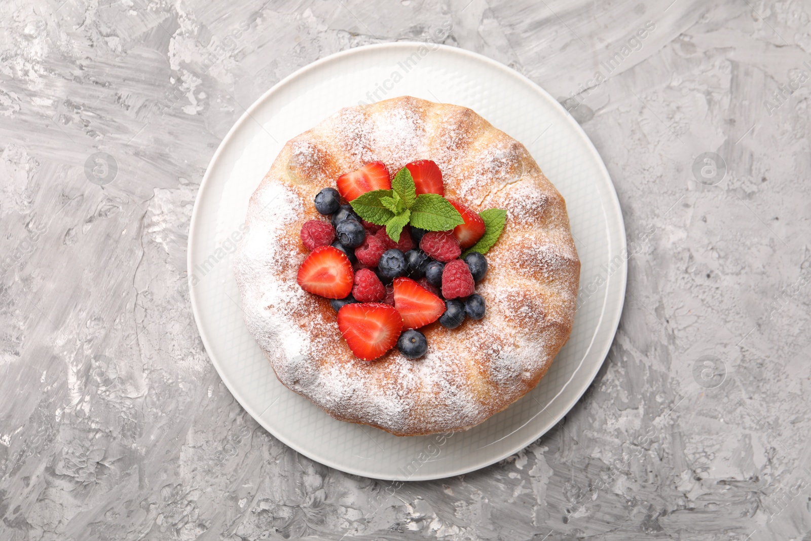 Tasty Bundt cake with powdered sugar and berries on grey textured table, top view Photo of Tasty Bundt cake with powdered sugar and berries on grey textured table, top view