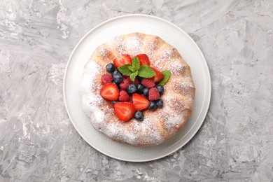 Photo of Tasty Bundt cake with powdered sugar and berries on grey textured table, top view