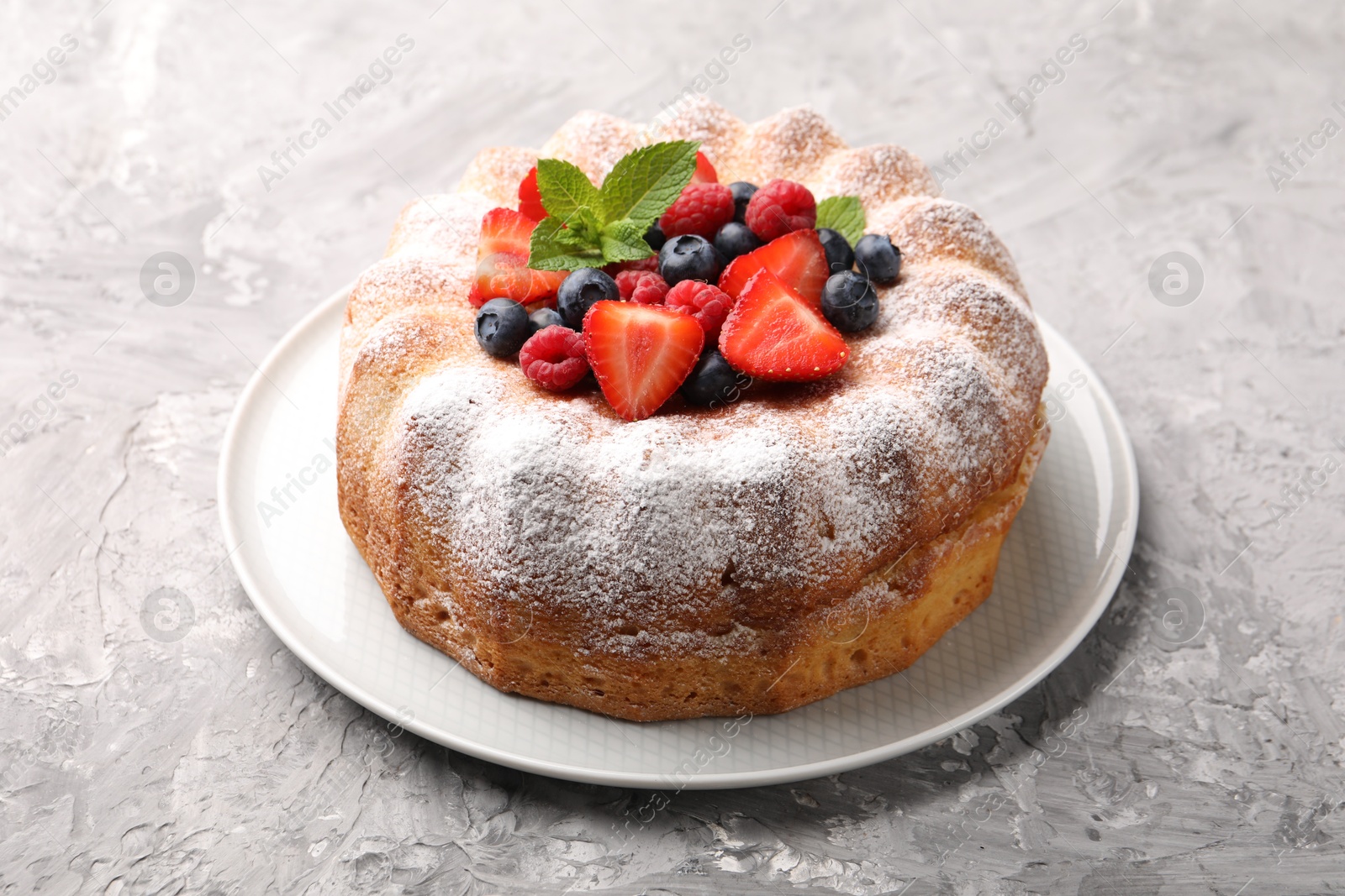 Tasty Bundt cake with powdered sugar and berries on grey textured table Photo of Tasty Bundt cake with powdered sugar and berries on grey textured table