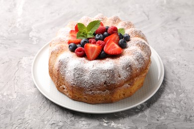 Photo of Tasty Bundt cake with powdered sugar and berries on grey textured table