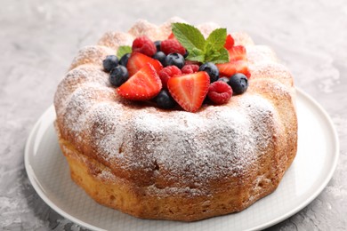 Photo of Tasty Bundt cake with powdered sugar and berries on grey textured table, closeup