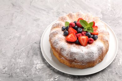 Photo of Tasty Bundt cake with powdered sugar and berries on grey textured table, space for text